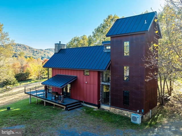 back of house featuring a chimney, metal roof, a deck with mountain view, a standing seam roof, and board and batten siding