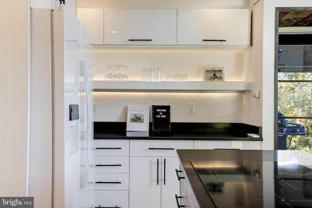 kitchen with dark countertops, modern cabinets, black cooktop, white fridge with ice dispenser, and white cabinetry