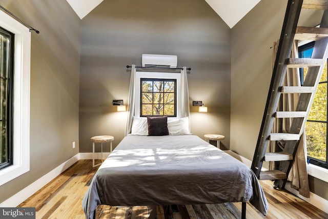 bedroom with high vaulted ceiling, an AC wall unit, light wood-style flooring, and baseboards