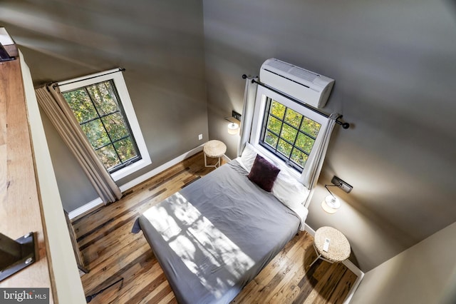 bedroom featuring multiple windows, a wall unit AC, wood finished floors, and baseboards