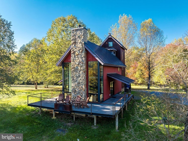 rear view of house featuring a standing seam roof, a chimney, metal roof, and an outbuilding