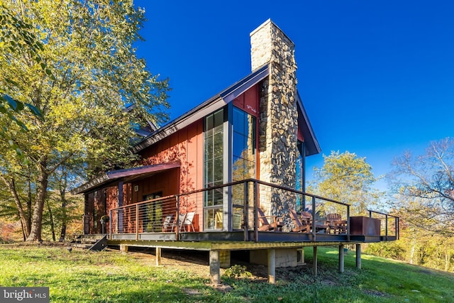 back of property with a chimney, a wooden deck, and a lawn