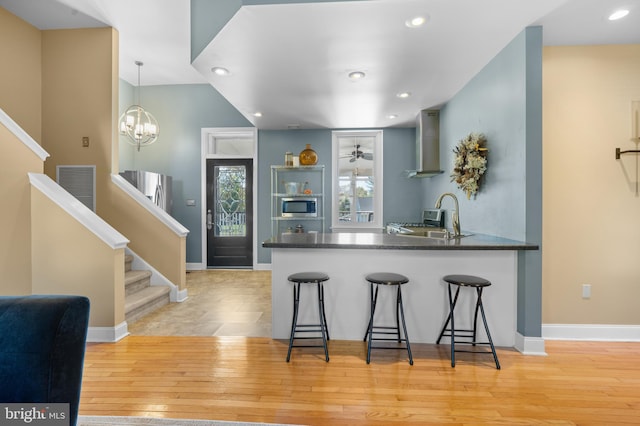 kitchen with wall chimney exhaust hood, hanging light fixtures, light hardwood / wood-style flooring, kitchen peninsula, and a breakfast bar area