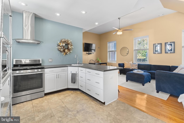 kitchen with sink, wall chimney range hood, stainless steel range oven, kitchen peninsula, and white cabinets