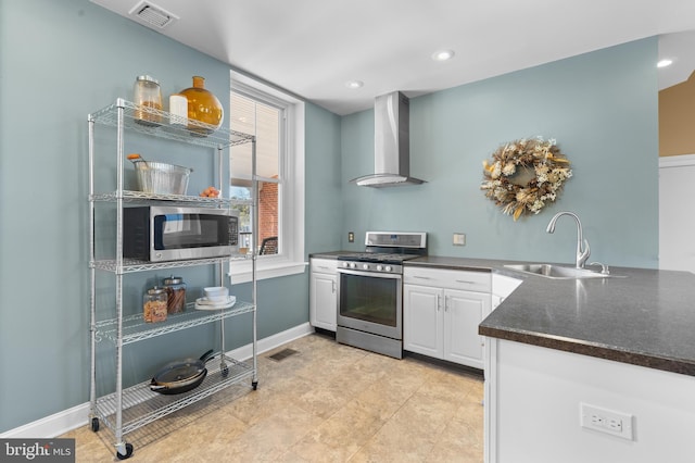 kitchen featuring appliances with stainless steel finishes, sink, wall chimney range hood, light tile patterned floors, and white cabinets