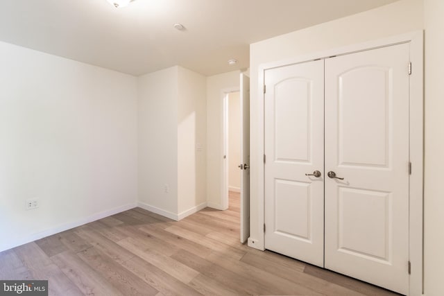 unfurnished bedroom with baseboards, light wood finished floors, and a closet