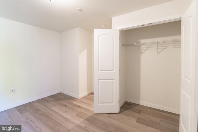 unfurnished bedroom featuring baseboards, a closet, and light wood-style flooring