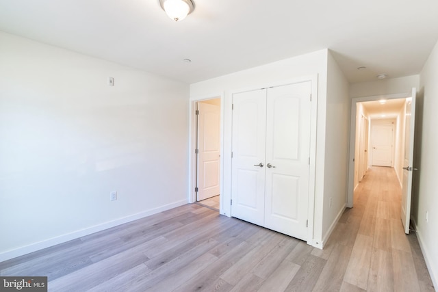 unfurnished bedroom featuring baseboards, light wood-style floors, and a closet