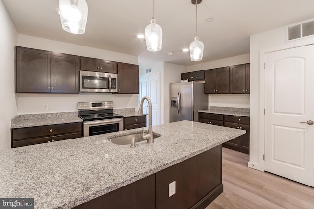 kitchen with pendant lighting, sink, appliances with stainless steel finishes, dark brown cabinets, and light stone counters