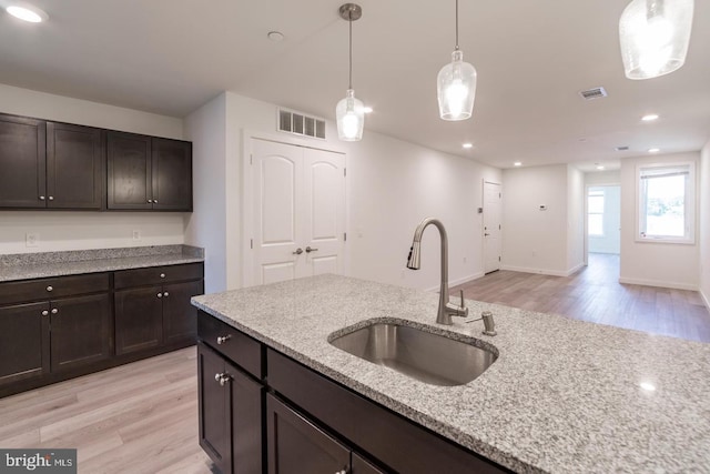 kitchen with decorative light fixtures, sink, dark brown cabinetry, light stone counters, and light hardwood / wood-style flooring