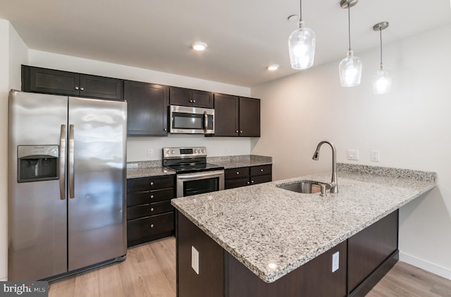 kitchen with light stone counters, a sink, a peninsula, light wood-style floors, and stainless steel appliances