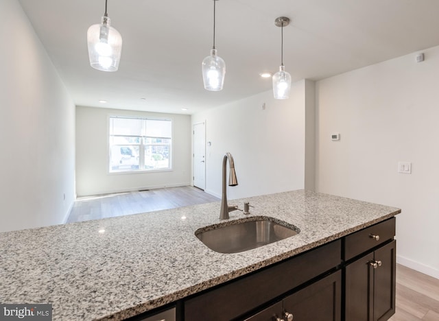 kitchen with light wood finished floors, dark brown cabinets, light stone countertops, and a sink