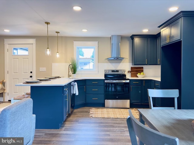 kitchen with blue cabinets, stainless steel appliances, wall chimney exhaust hood, pendant lighting, and dark wood-type flooring