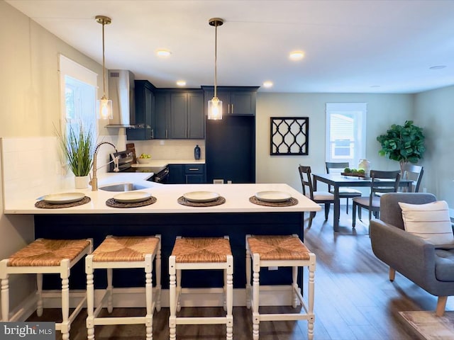 kitchen featuring wall chimney exhaust hood, a breakfast bar, hanging light fixtures, and dark hardwood / wood-style flooring