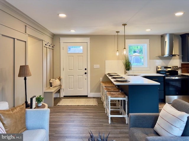 kitchen with a kitchen bar, wall chimney exhaust hood, stainless steel electric range, decorative light fixtures, and dark wood-type flooring