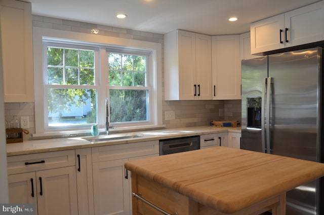 kitchen featuring dishwasher, sink, backsplash, stainless steel fridge, and white cabinets