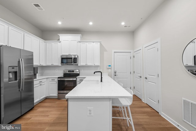 kitchen with decorative backsplash, light hardwood / wood-style flooring, light stone countertops, white cabinets, and appliances with stainless steel finishes