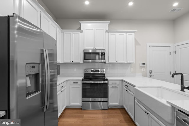 kitchen with sink, hardwood / wood-style floors, white cabinetry, appliances with stainless steel finishes, and tasteful backsplash