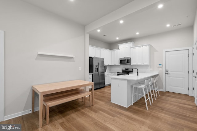 kitchen with white cabinetry, appliances with stainless steel finishes, light hardwood / wood-style flooring, and kitchen peninsula