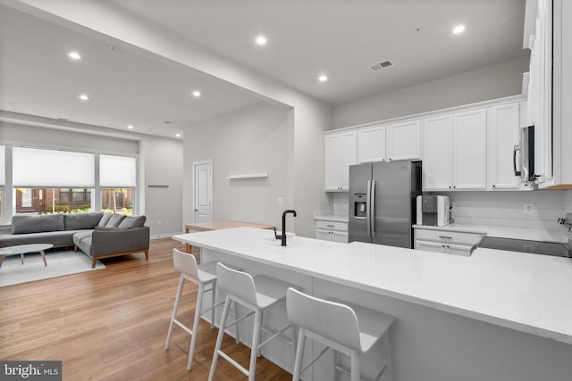 kitchen featuring backsplash, appliances with stainless steel finishes, a breakfast bar area, white cabinetry, and light wood-type flooring