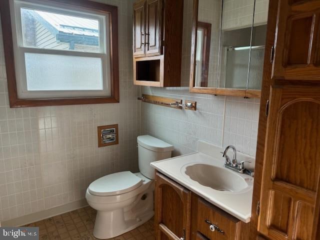 bathroom featuring vanity, toilet, tile walls, and walk in shower