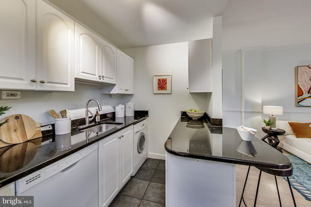 kitchen featuring dark tile patterned floors, dishwasher, washer / dryer, sink, and white cabinetry