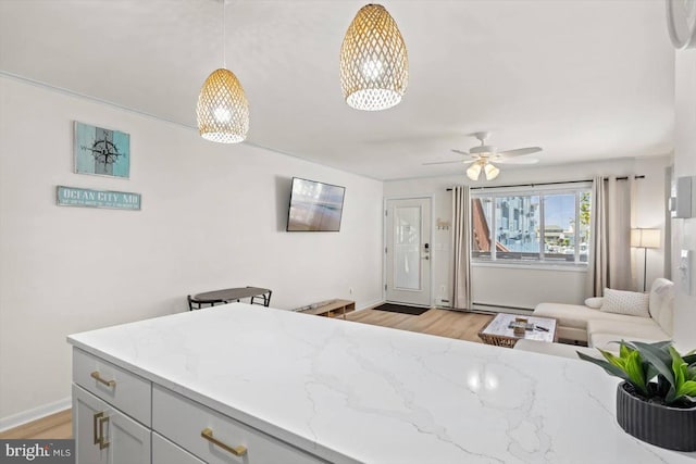 kitchen with light stone counters, decorative light fixtures, light wood-type flooring, and ceiling fan