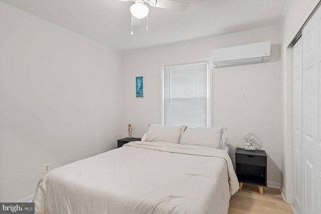 bedroom with an AC wall unit, a closet, ceiling fan, light hardwood / wood-style floors, and ornamental molding