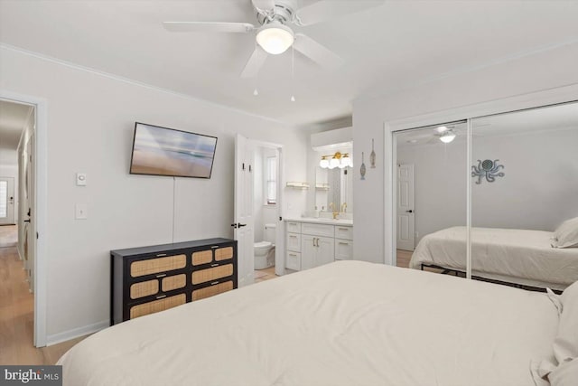 bedroom featuring a closet, ensuite bath, light wood-type flooring, and ceiling fan