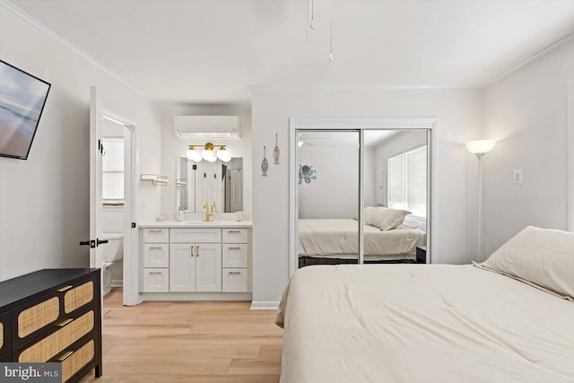 bedroom featuring connected bathroom, a closet, a wall mounted air conditioner, crown molding, and light hardwood / wood-style floors