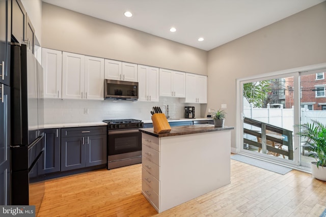 kitchen with stainless steel appliances, a kitchen island, tasteful backsplash, light hardwood / wood-style flooring, and white cabinets