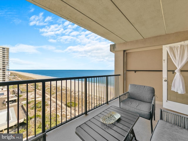 balcony with a water view, a view of the beach, and radiator heating unit