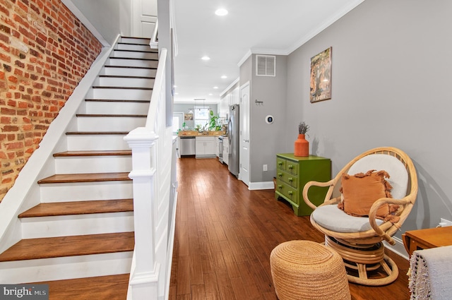 stairs featuring brick wall, hardwood / wood-style floors, and crown molding