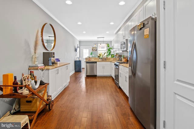 kitchen featuring appliances with stainless steel finishes, kitchen peninsula, hanging light fixtures, hardwood / wood-style floors, and white cabinets