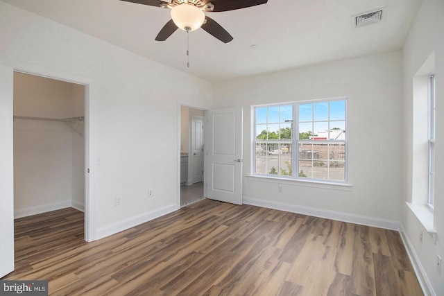 unfurnished bedroom featuring a closet, a spacious closet, dark wood-type flooring, and ceiling fan