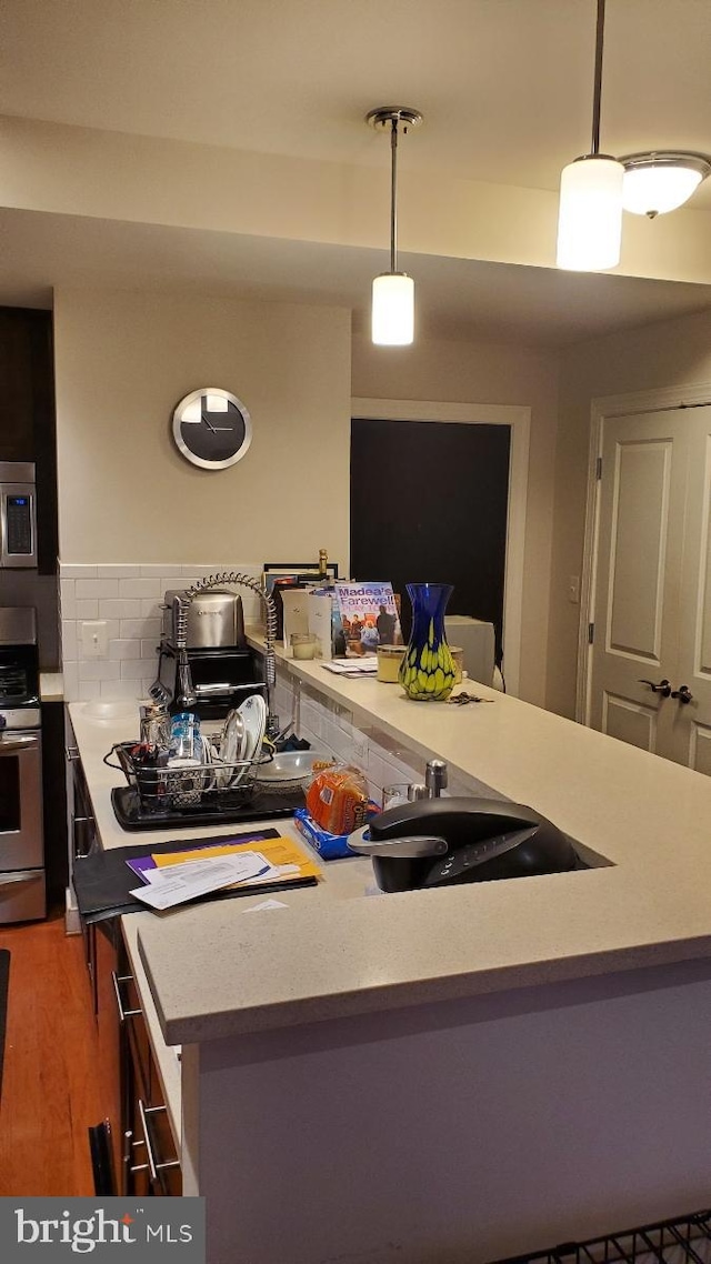 kitchen with backsplash, appliances with stainless steel finishes, decorative light fixtures, and dark hardwood / wood-style flooring