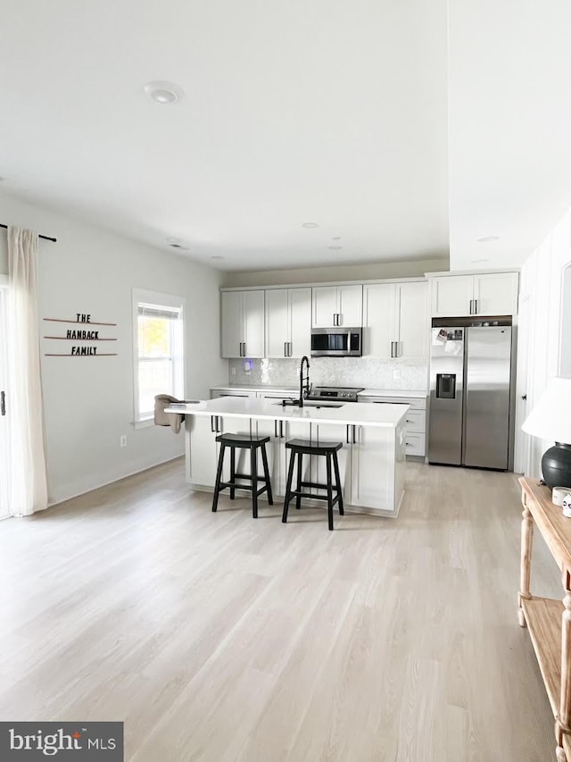 kitchen featuring appliances with stainless steel finishes, light wood-type flooring, white cabinetry, a breakfast bar area, and a center island with sink