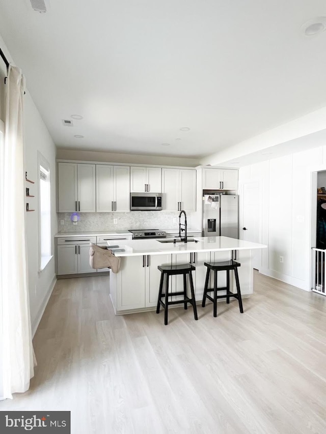 kitchen featuring a kitchen breakfast bar, stainless steel appliances, light wood-type flooring, and an island with sink