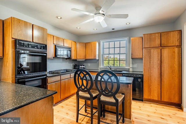 kitchen with dark stone counters, black appliances, sink, ceiling fan, and light hardwood / wood-style flooring