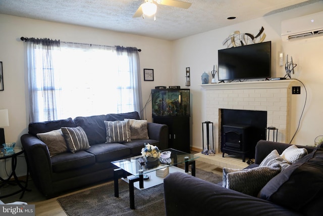 living room featuring a wall mounted air conditioner, a wood stove, hardwood / wood-style floors, a textured ceiling, and ceiling fan