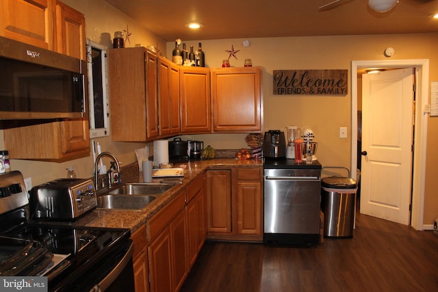 kitchen with appliances with stainless steel finishes, sink, dark stone counters, and dark hardwood / wood-style flooring