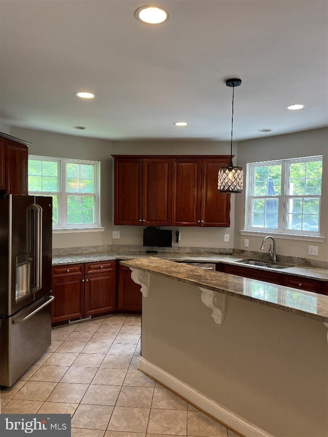 kitchen featuring high end refrigerator, sink, pendant lighting, light tile patterned floors, and light stone counters