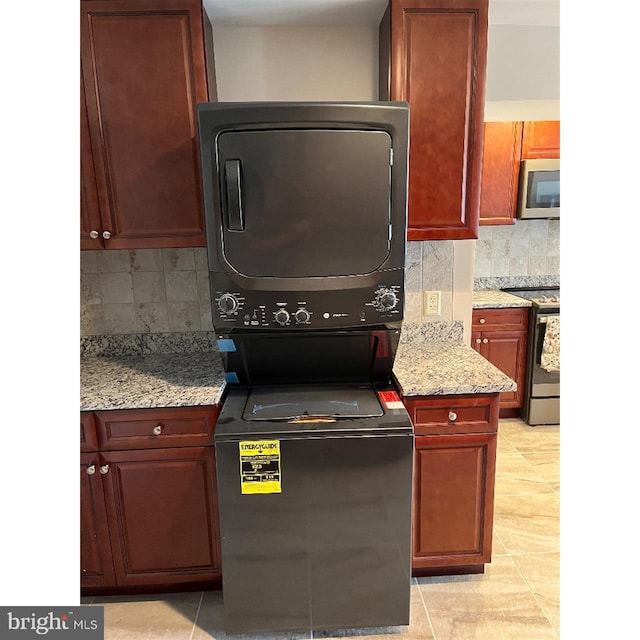 kitchen featuring light stone countertops, light tile patterned flooring, backsplash, stainless steel appliances, and stacked washer / drying machine