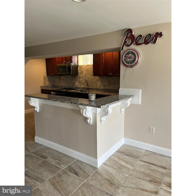 kitchen featuring kitchen peninsula, dark stone counters, backsplash, and a breakfast bar area