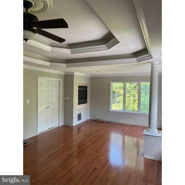 unfurnished living room featuring wood-type flooring, decorative columns, crown molding, a raised ceiling, and ceiling fan