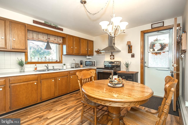 kitchen featuring light wood-type flooring, wall chimney exhaust hood, appliances with stainless steel finishes, and pendant lighting