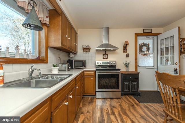 kitchen with wall chimney range hood, backsplash, sink, appliances with stainless steel finishes, and dark hardwood / wood-style flooring