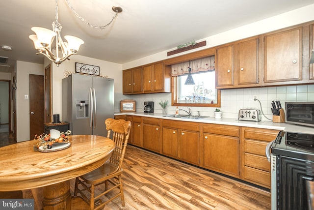 kitchen with sink, light wood-type flooring, range, stainless steel fridge with ice dispenser, and a chandelier