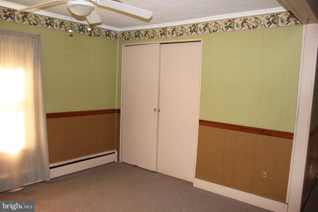 unfurnished bedroom featuring a baseboard heating unit, ceiling fan, carpet flooring, a closet, and wooden walls