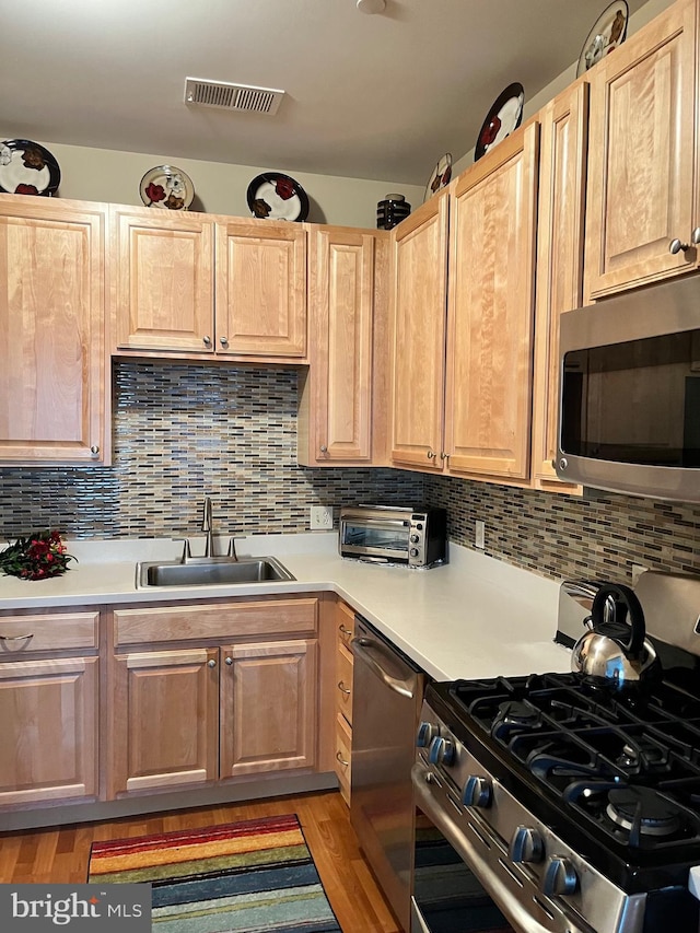 kitchen featuring appliances with stainless steel finishes, sink, backsplash, and light wood-type flooring